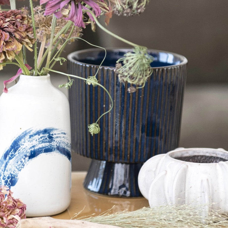 Dark blue fluted planter on wooden table with vase and other decorative items around