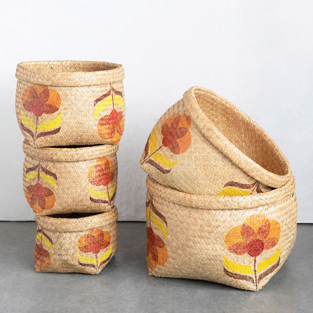 5 seagrass baskets with orange flowers and yellow leaves and rolled rim on grey floor and grey background.