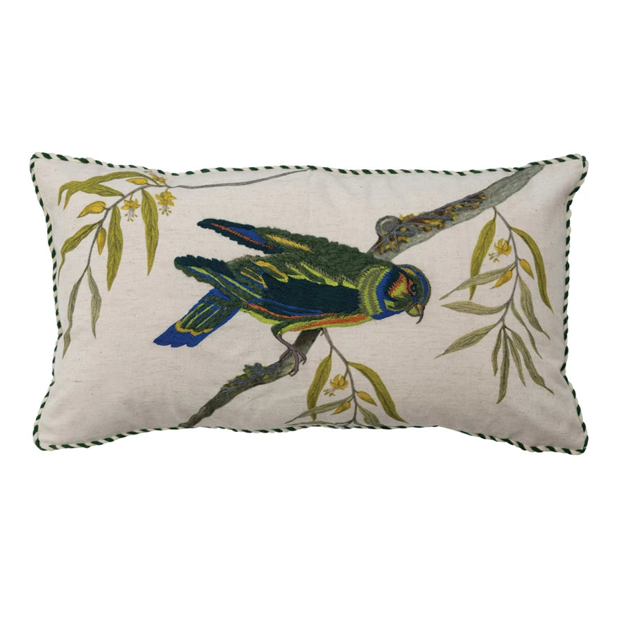 white pillow with blue and green embroidered bird standing on a branch on white background.