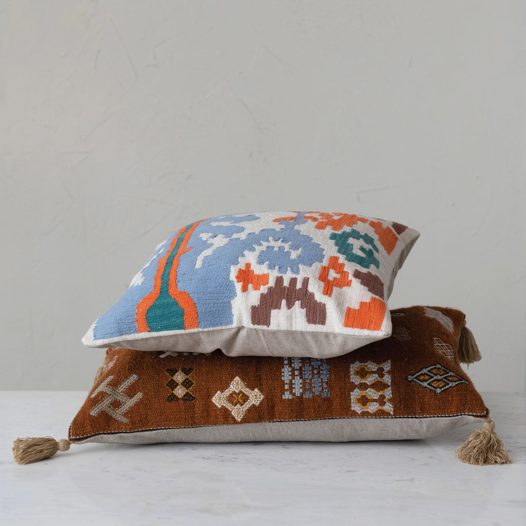 18in Embroidered Ikat & Chambray Pillow with blue, orange, brown, and green on top of brown pillow