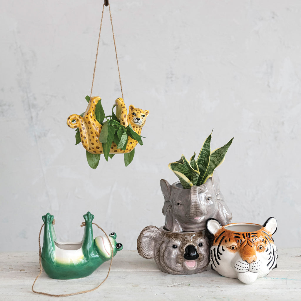 Ceramic Koala, Elephant, and Tiger Head Planters stacked next to hanging frog and leopard planters on grey table.