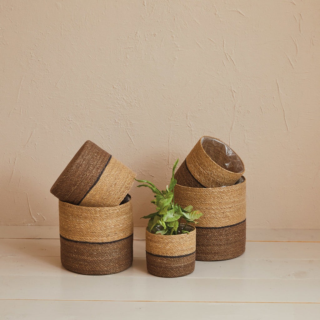 Two Toned Jute Baskets in different sizes stacked together and one with a plant inside against a tan colored wall