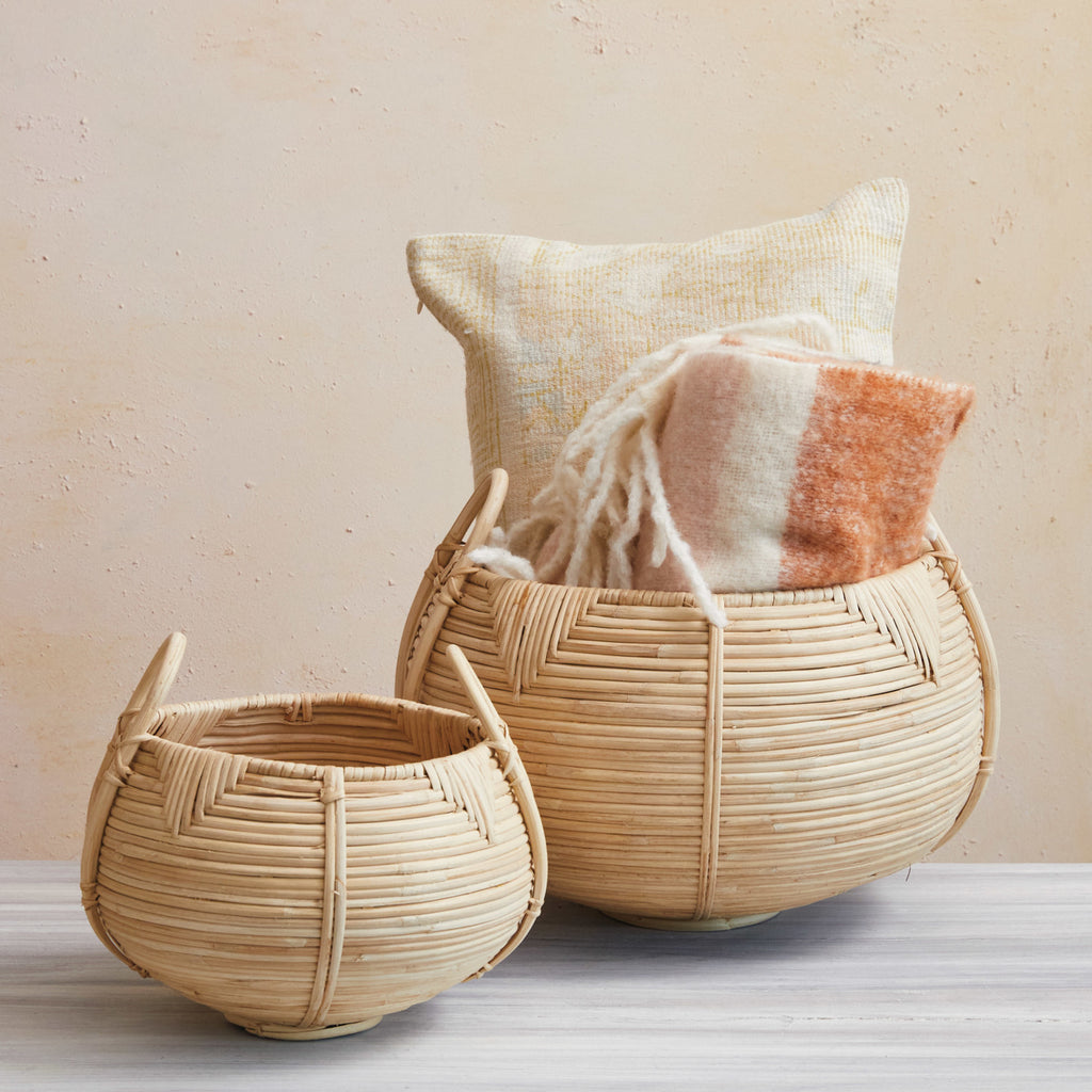 Round Hand-Woven Rattan Baskets with Handles and triangle and round woven pattern one smaller than the other with blankets and pillows inside.