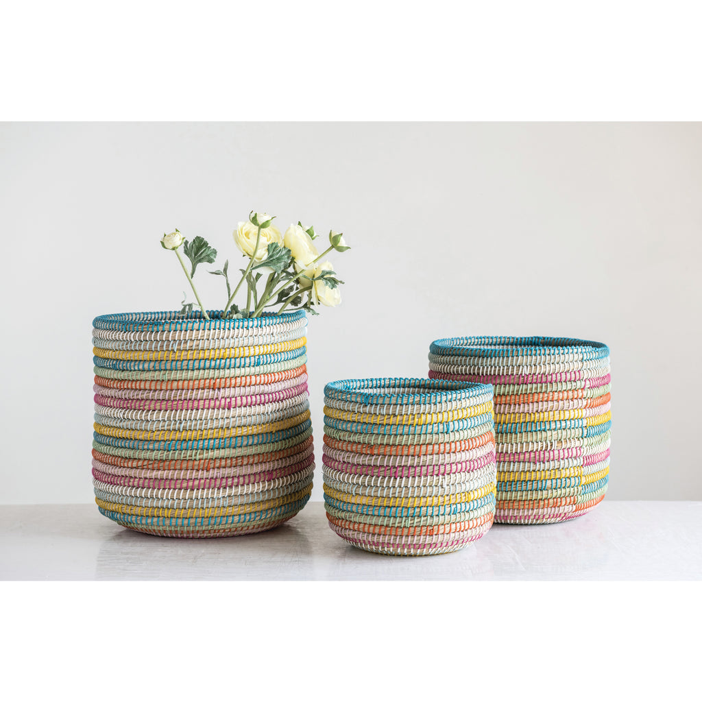 10-13in Hand-Woven Grass Baskets with rainbow colored twine. Shown with white flowers on grey background.